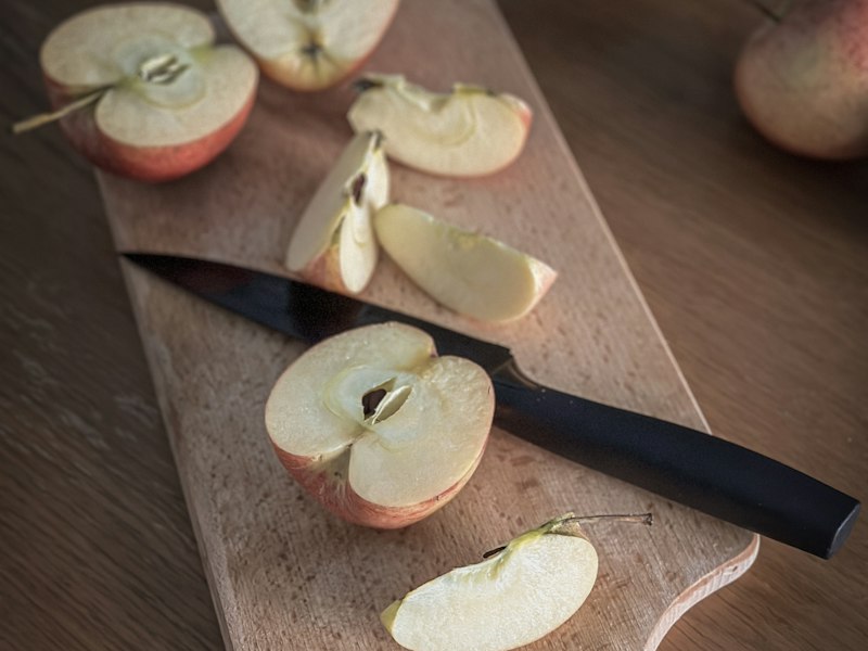 Apples being sliced on a wooden cutting board